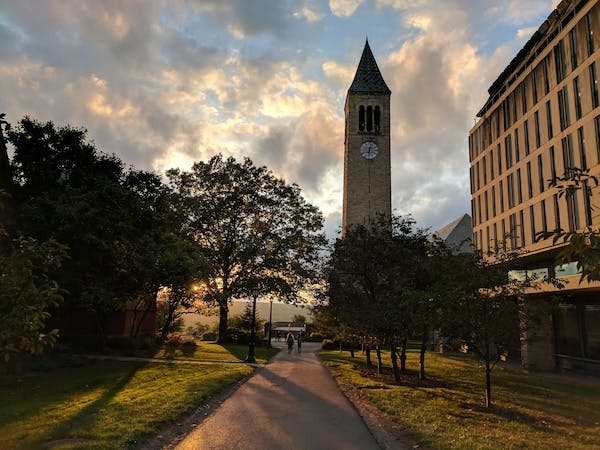 McGraw Clock Tower at Cornell University framed by fall trees in the foreground and a setting sun in the background
